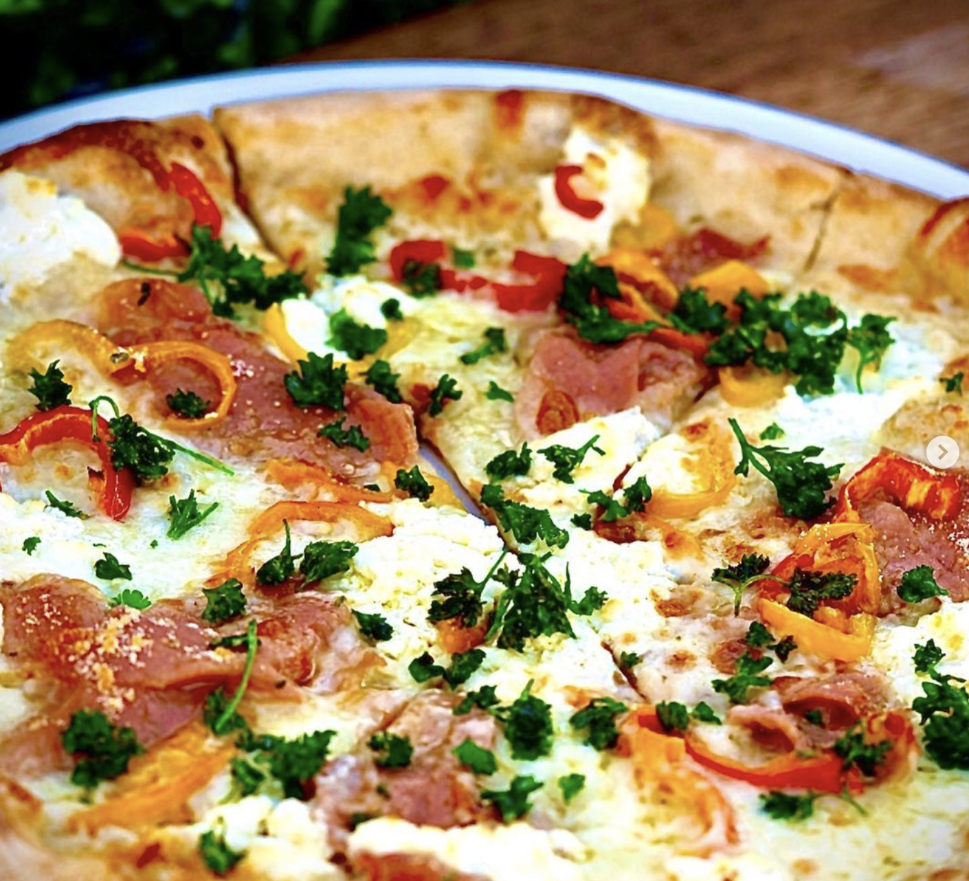 White wood-fired pizza with prosciutto, peppers, and herbs